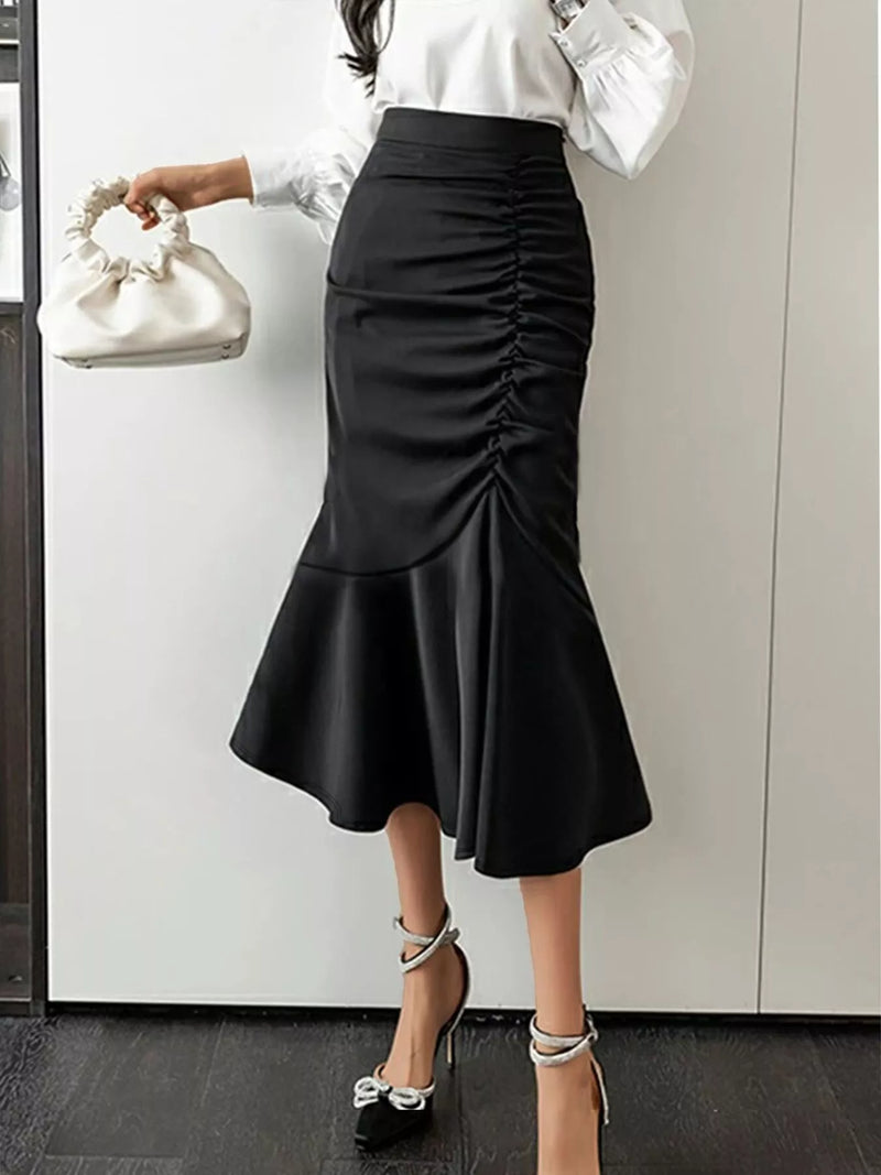 Person wearing a black ruched skirt with a white top and holding a white handbag.