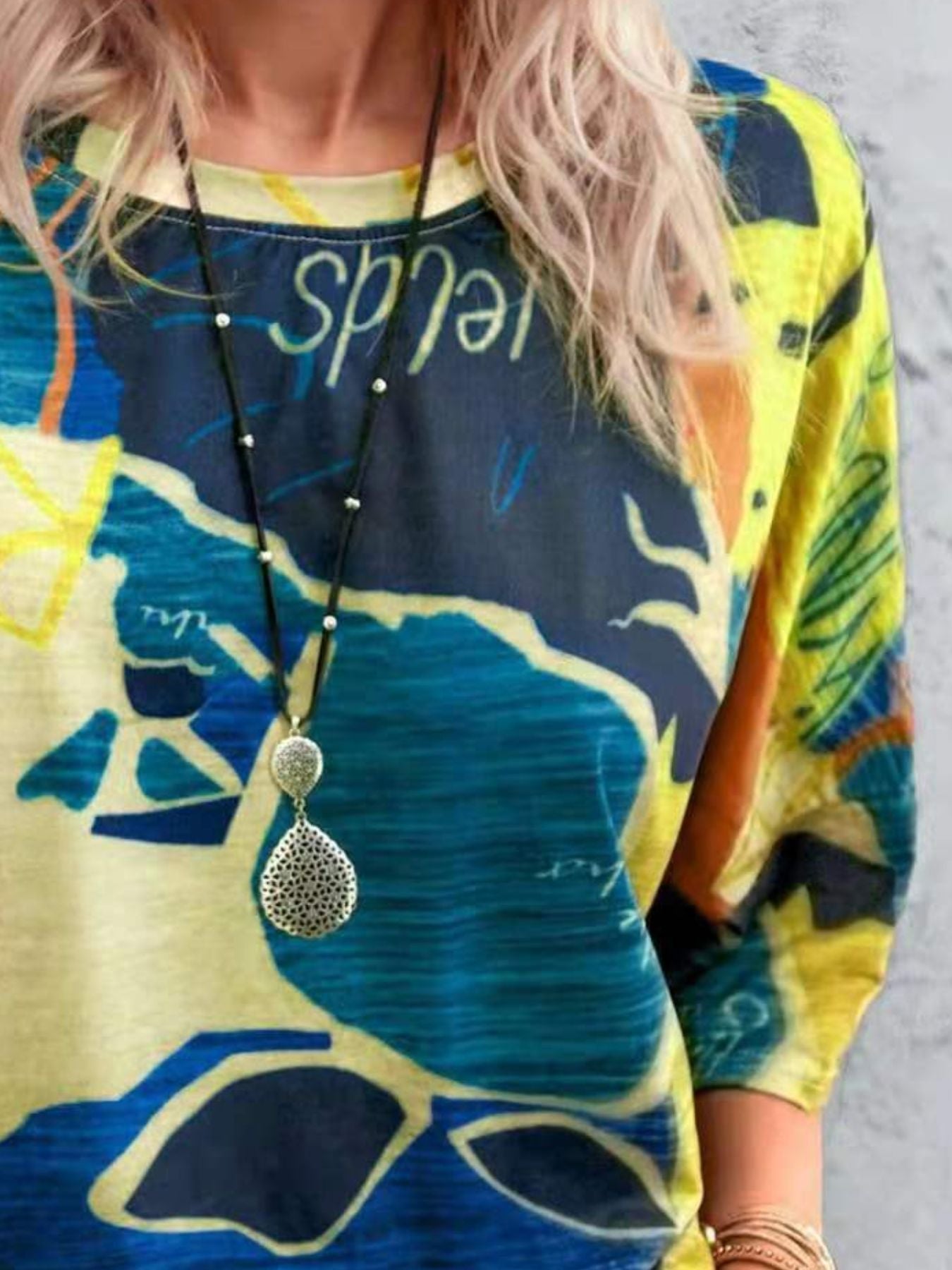 Person wearing a colorful dress with abstract patterns and a long necklace.
