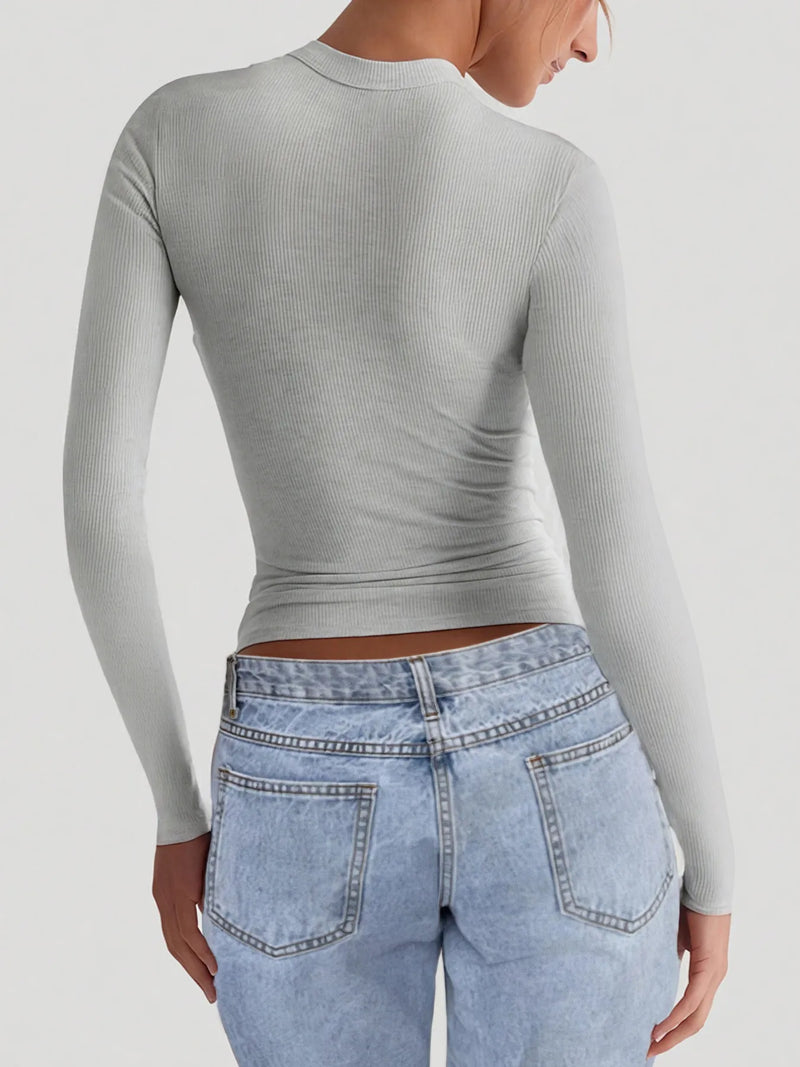Person wearing a gray ribbed long-sleeve top and light blue jeans on a white background