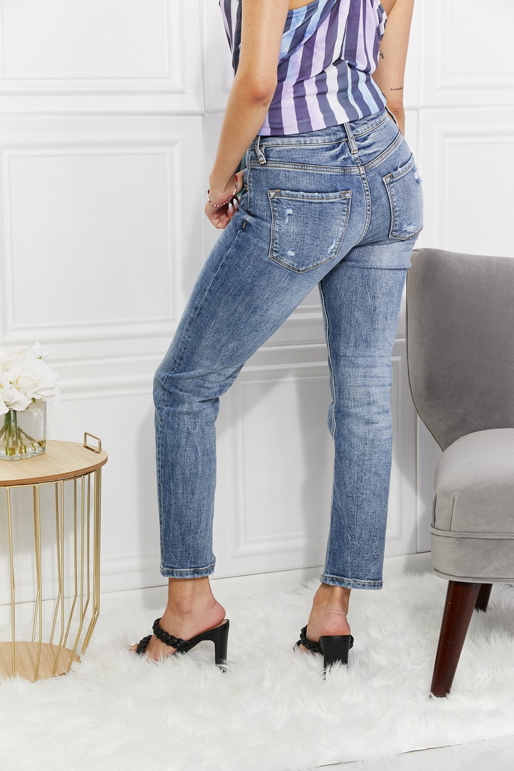 Person wearing blue jeans and a striped top in a room with a white wall and gray chair.