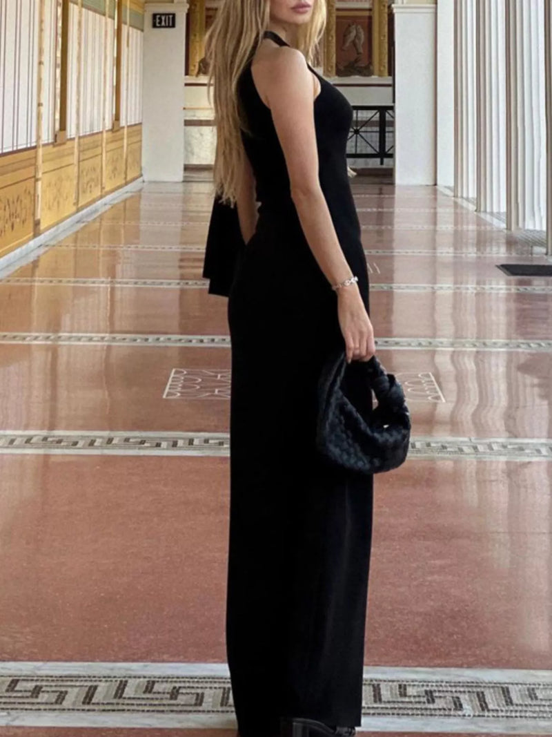 Woman in a black dress holding a matching handbag in an elegant interior setting.