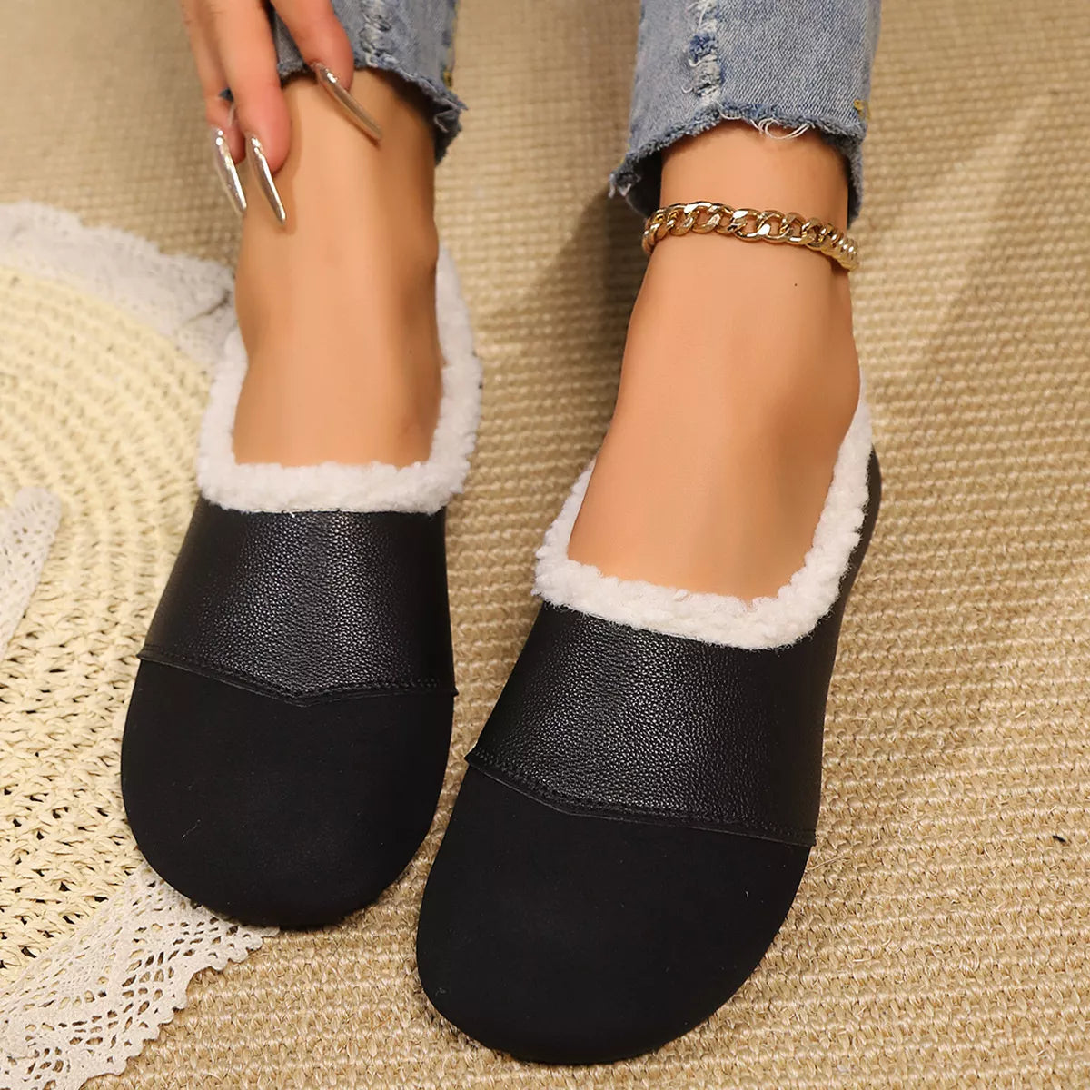 Black slip-on shoes with white lining worn by a person on a textured surface.