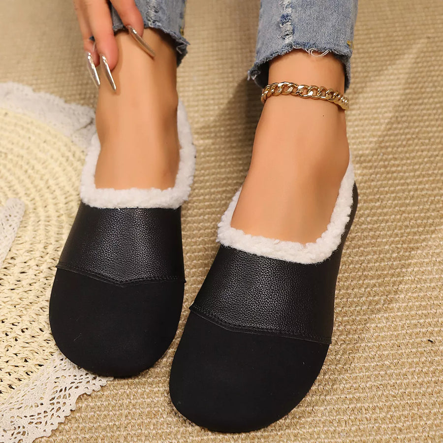 Black slip-on shoes with white lining worn by a person on a textured surface.