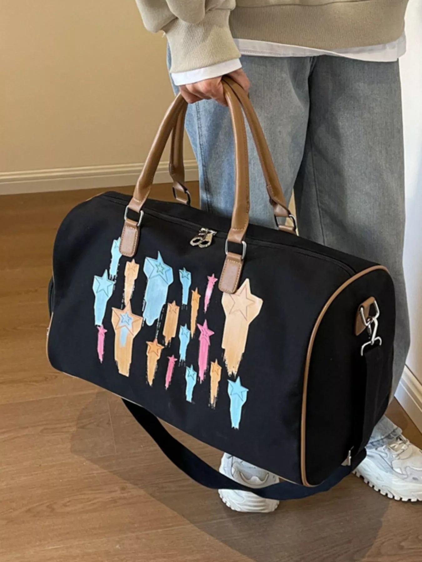 Person holding a black duffel bag with colorful dog illustrations on a wooden floor.