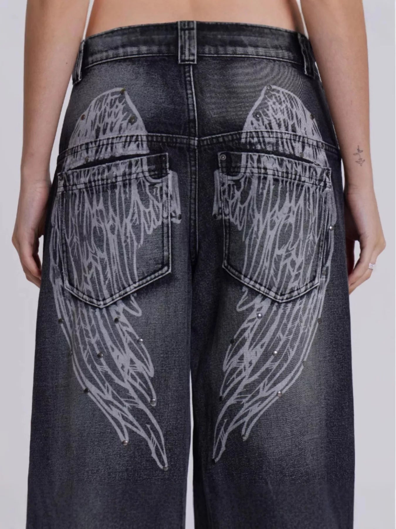 Black jeans with wing designs on the back pockets against a white background