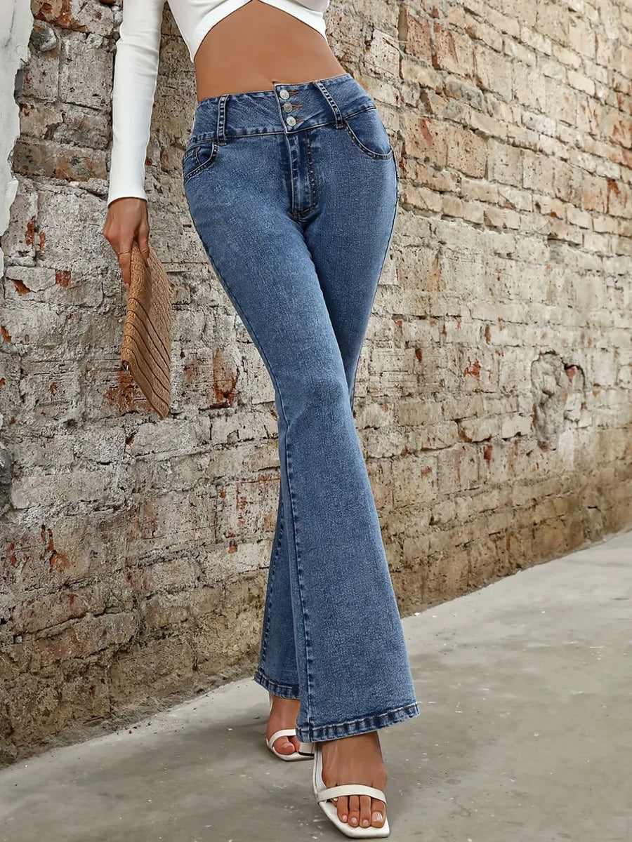 Person wearing blue flared jeans against a stone wall.