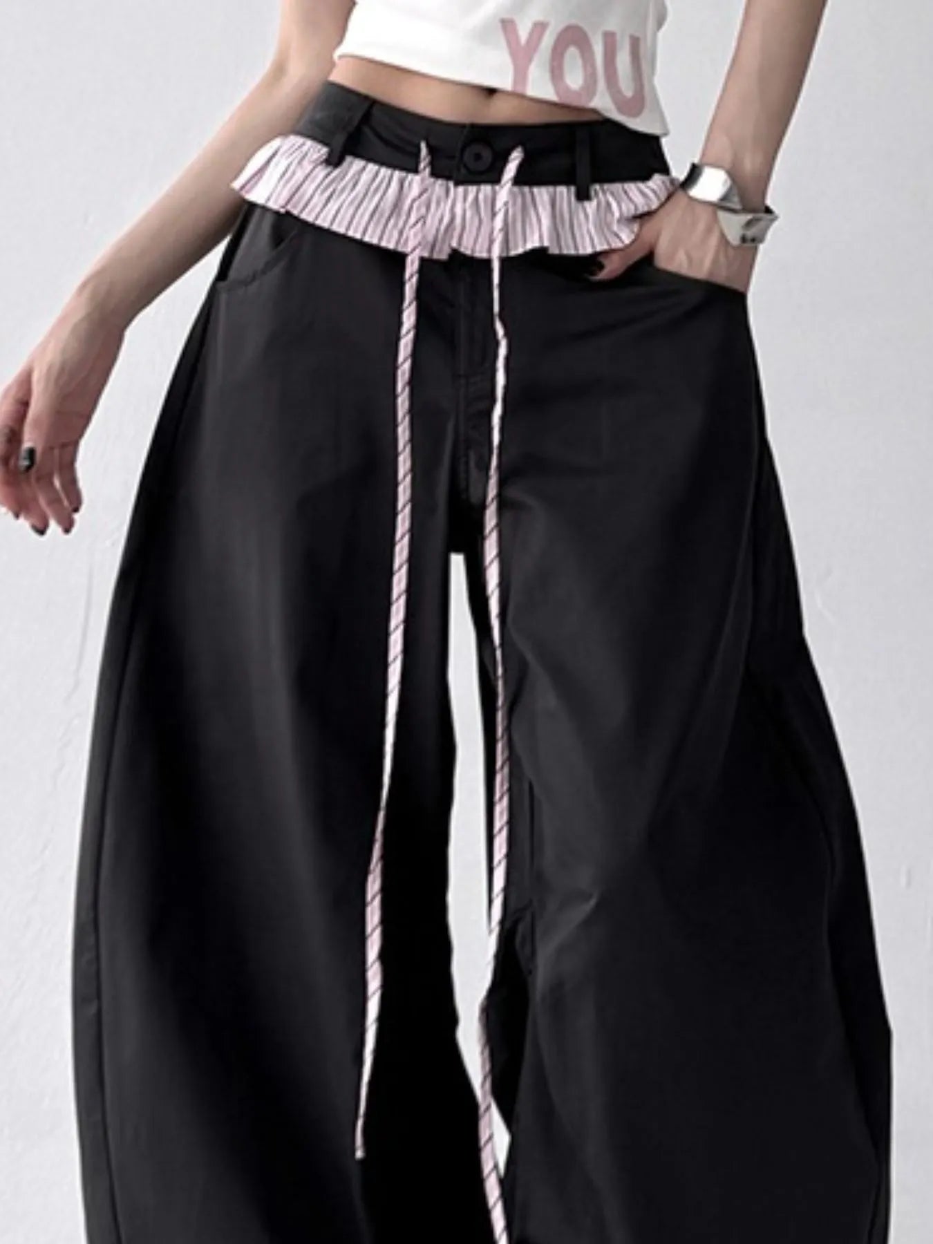 Person wearing black wide-leg pants with a ruffled waistband on a white background