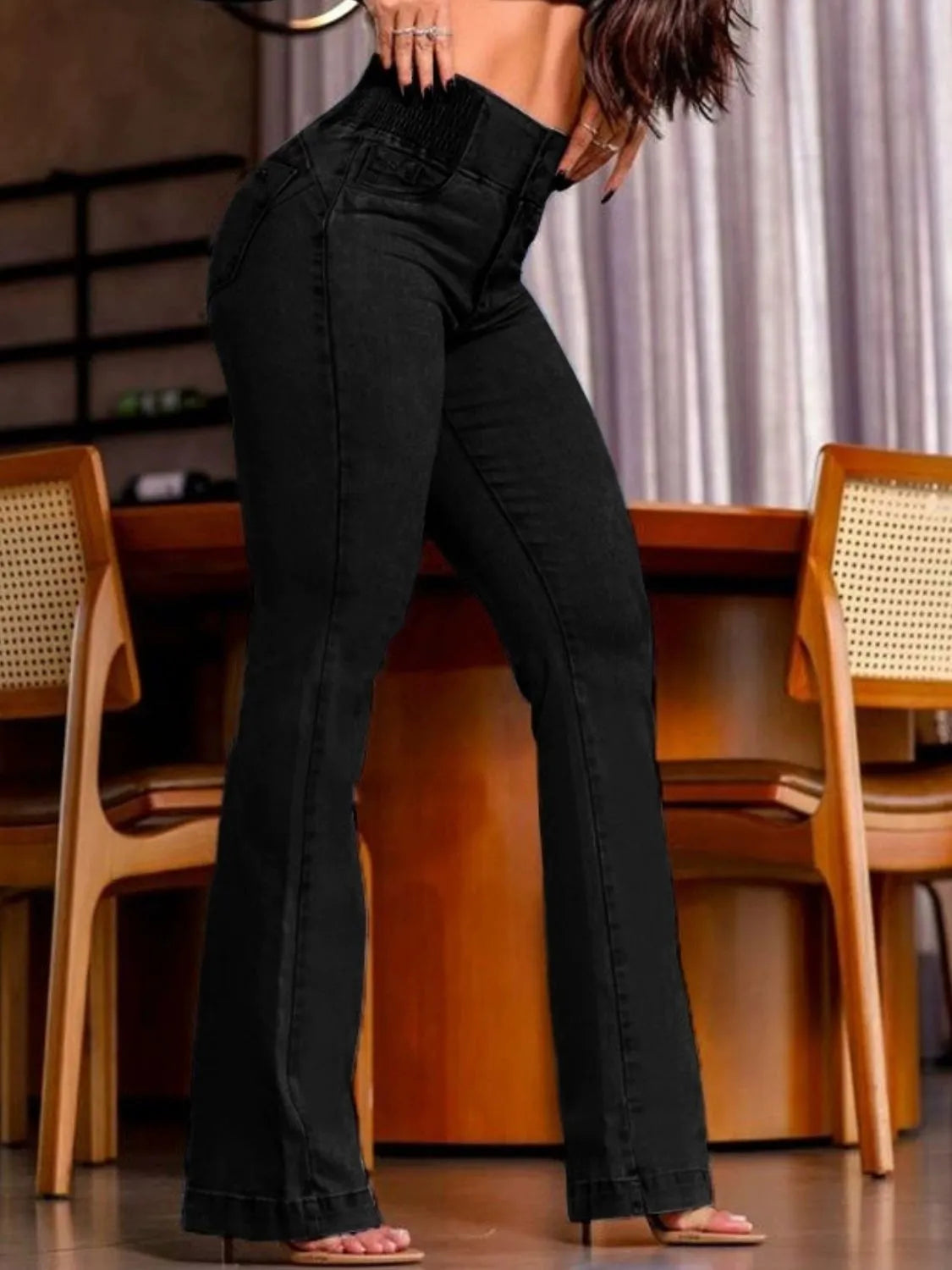 Person wearing black high-waisted jeans in a casual setting with wooden furniture.