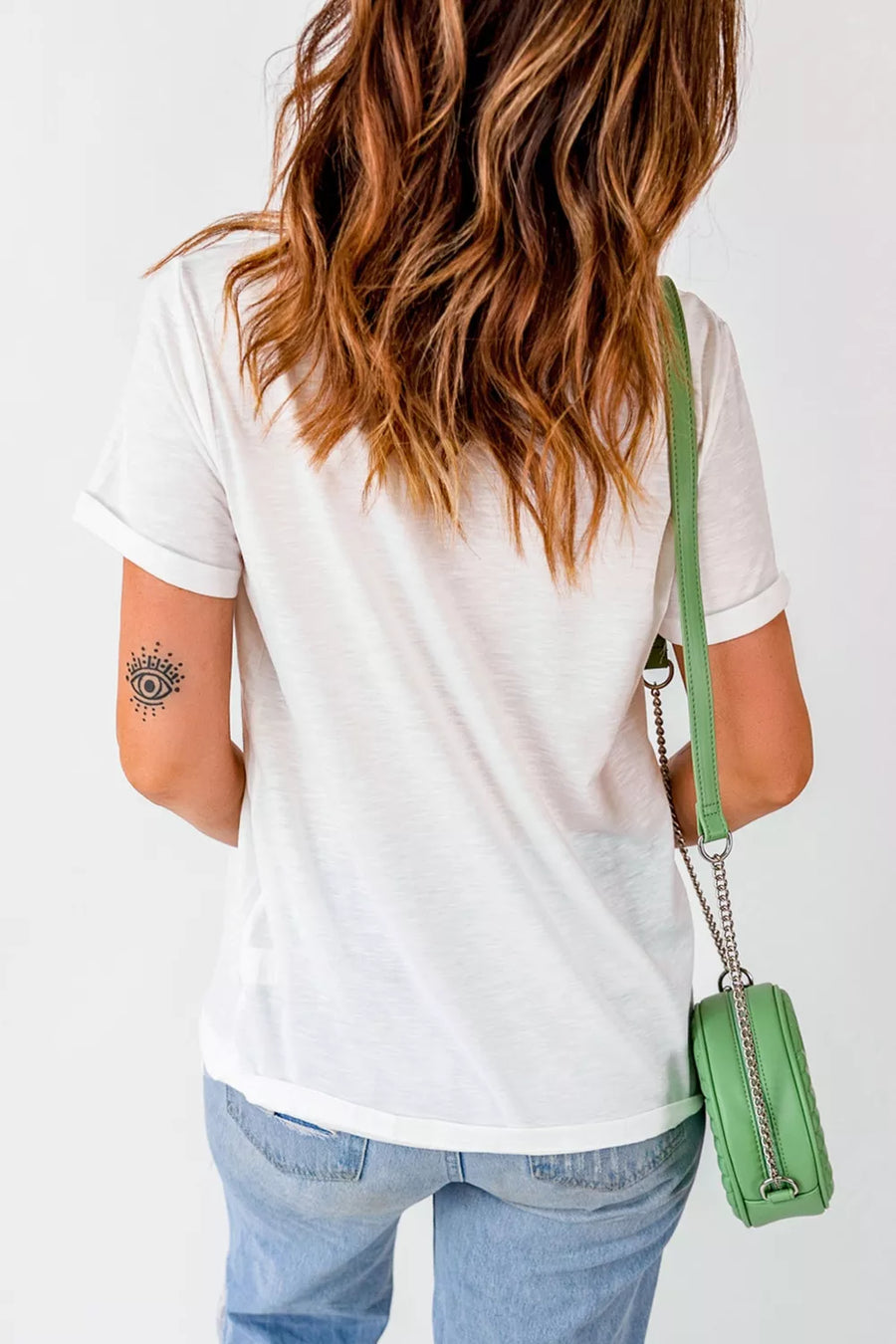 Person wearing a white t-shirt and blue jeans with a green handbag on a white background