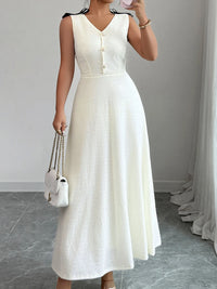 Woman wearing a white sleeveless dress holding a white handbag indoors.