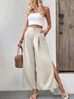 Woman wearing a white top and beige wide-leg pants, holding a straw bag against a wooden door background.