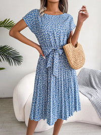 Woman wearing a blue floral dress holding a straw bag indoors.