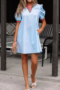 Woman wearing a light blue dress with colorful trim in an outdoor setting.