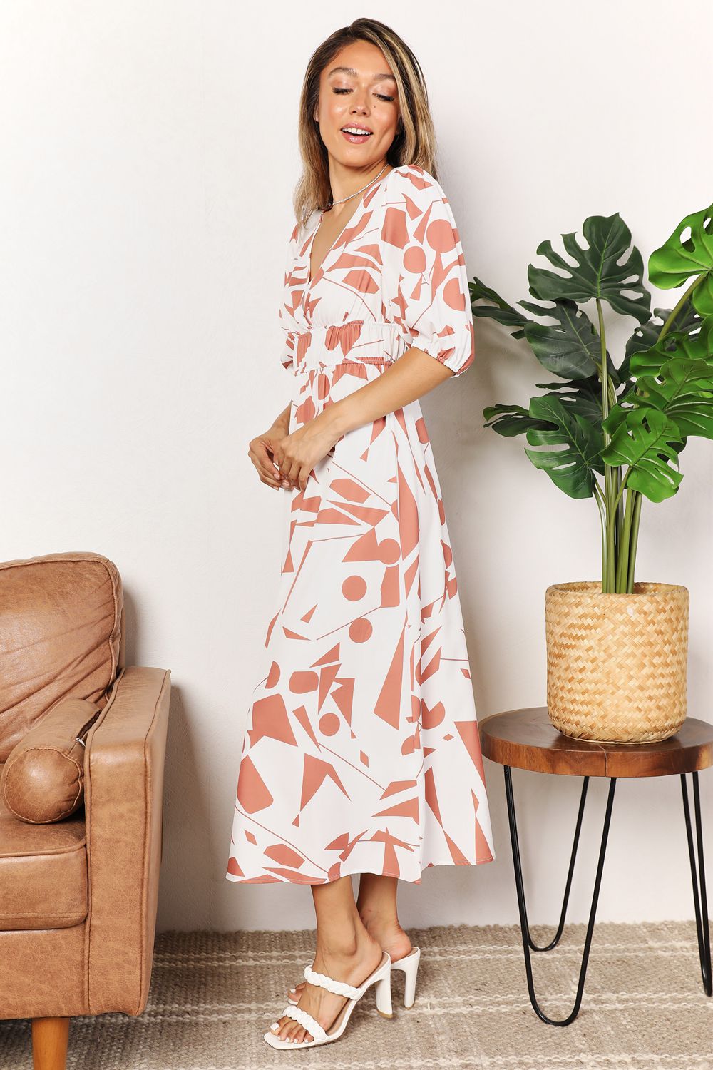 Woman in a floral dress standing in a living room with a plant and couch.