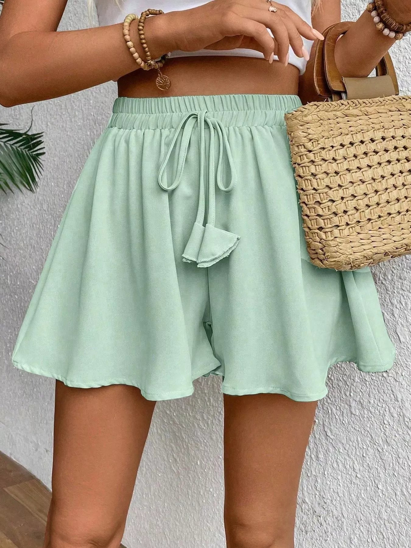 Person wearing light green shorts with a woven bag against a neutral background
