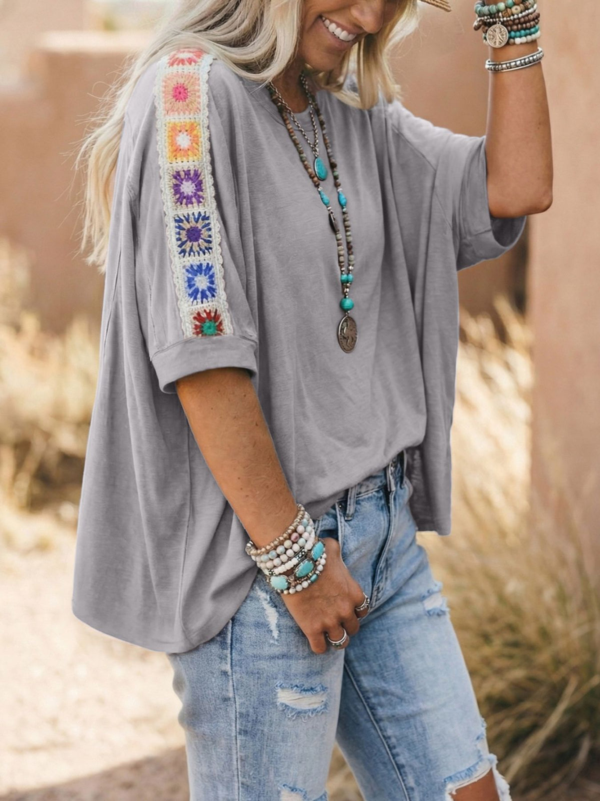 Person wearing a gray top with colorful embroidery and ripped jeans outdoors.