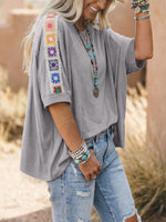 Person wearing a gray top with colorful embroidery and ripped jeans outdoors.