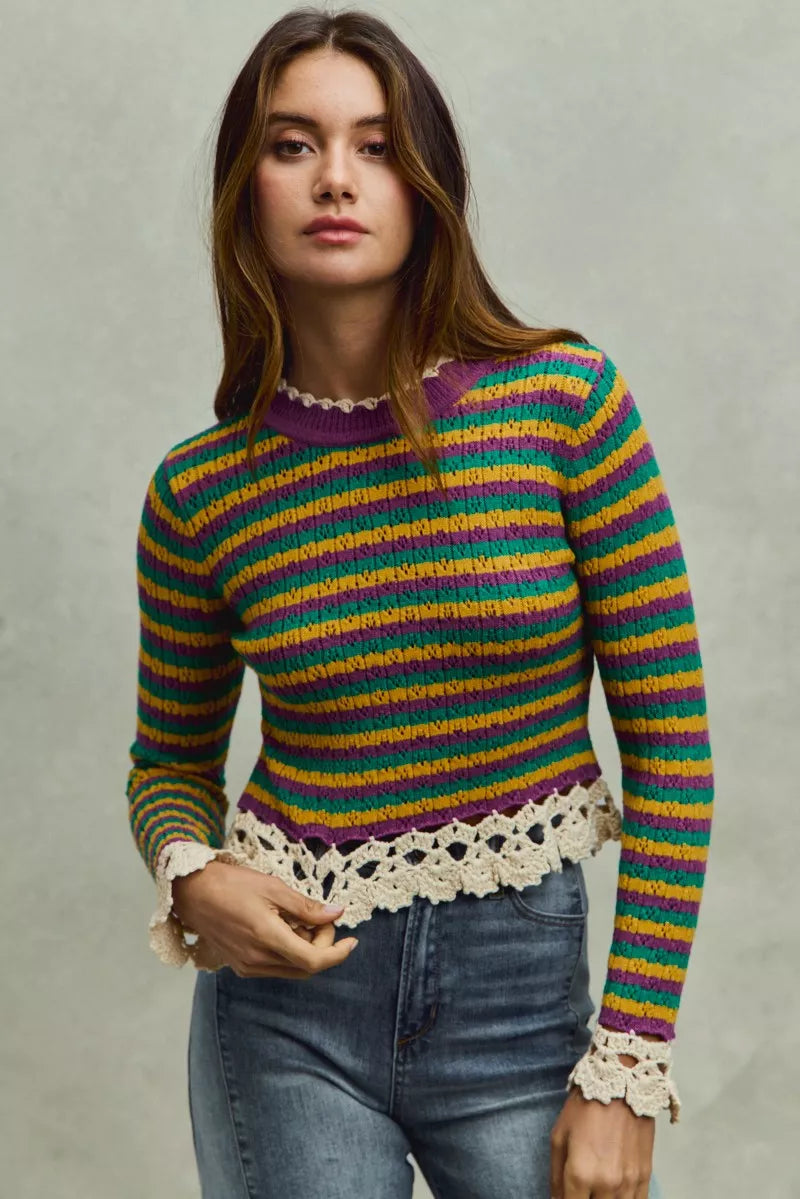 Woman wearing a colorful striped sweater with lace details on a plain background