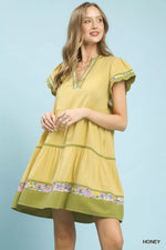 Woman wearing a yellow dress with floral embroidery on a light blue background