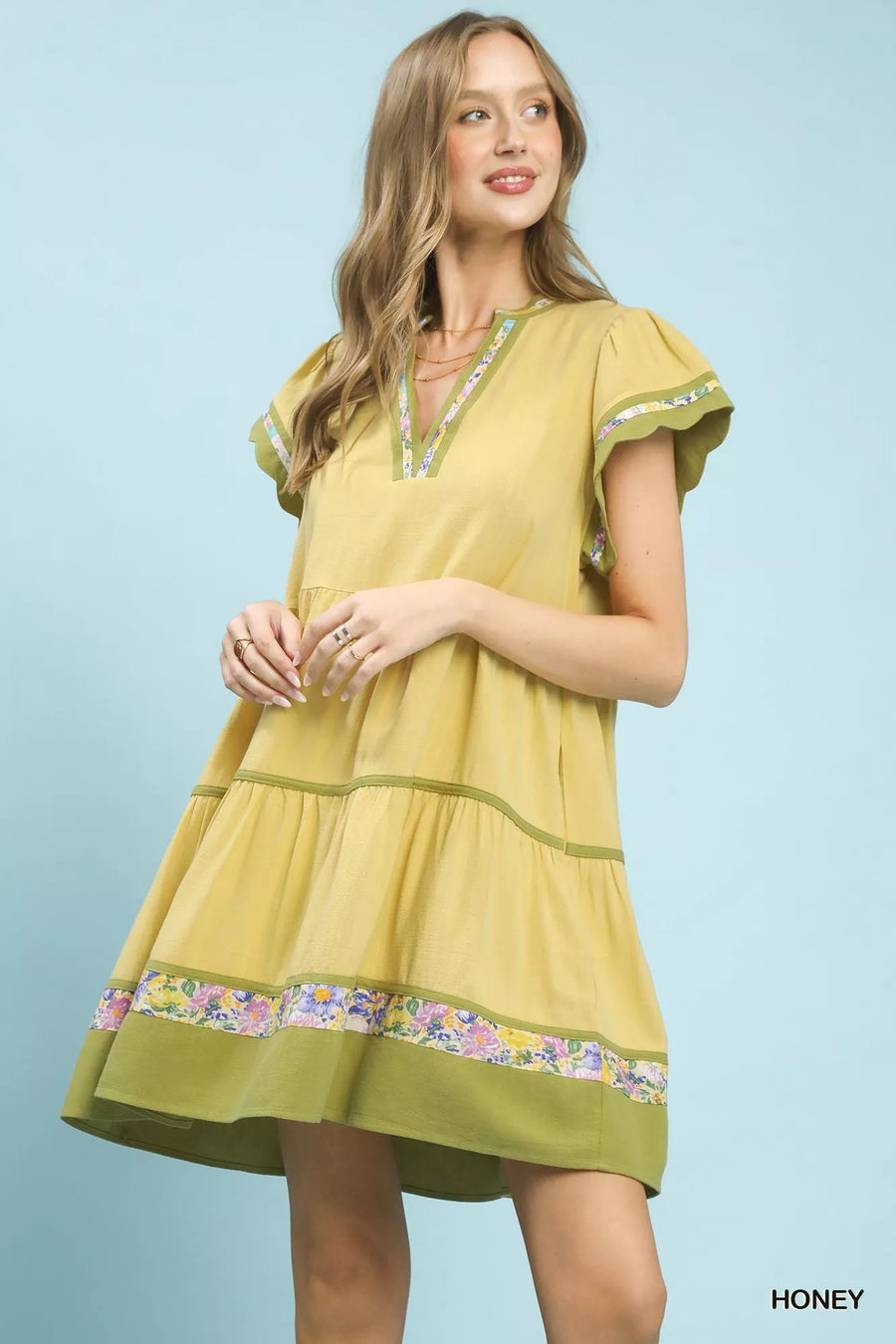 Woman wearing a yellow dress with floral embroidery on a light blue background