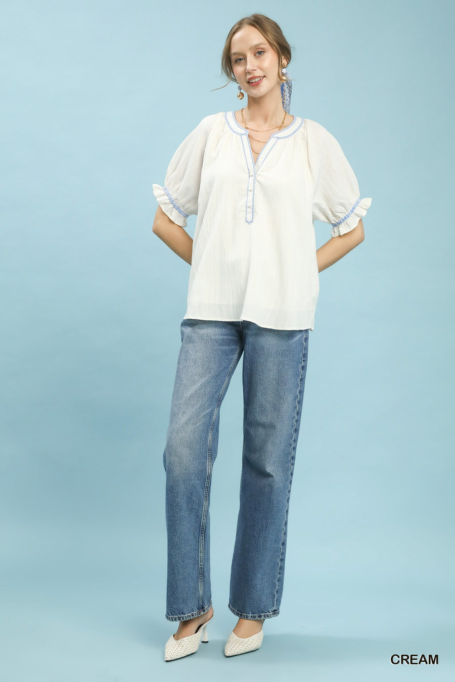 Woman wearing a white blouse and blue jeans against a light blue background