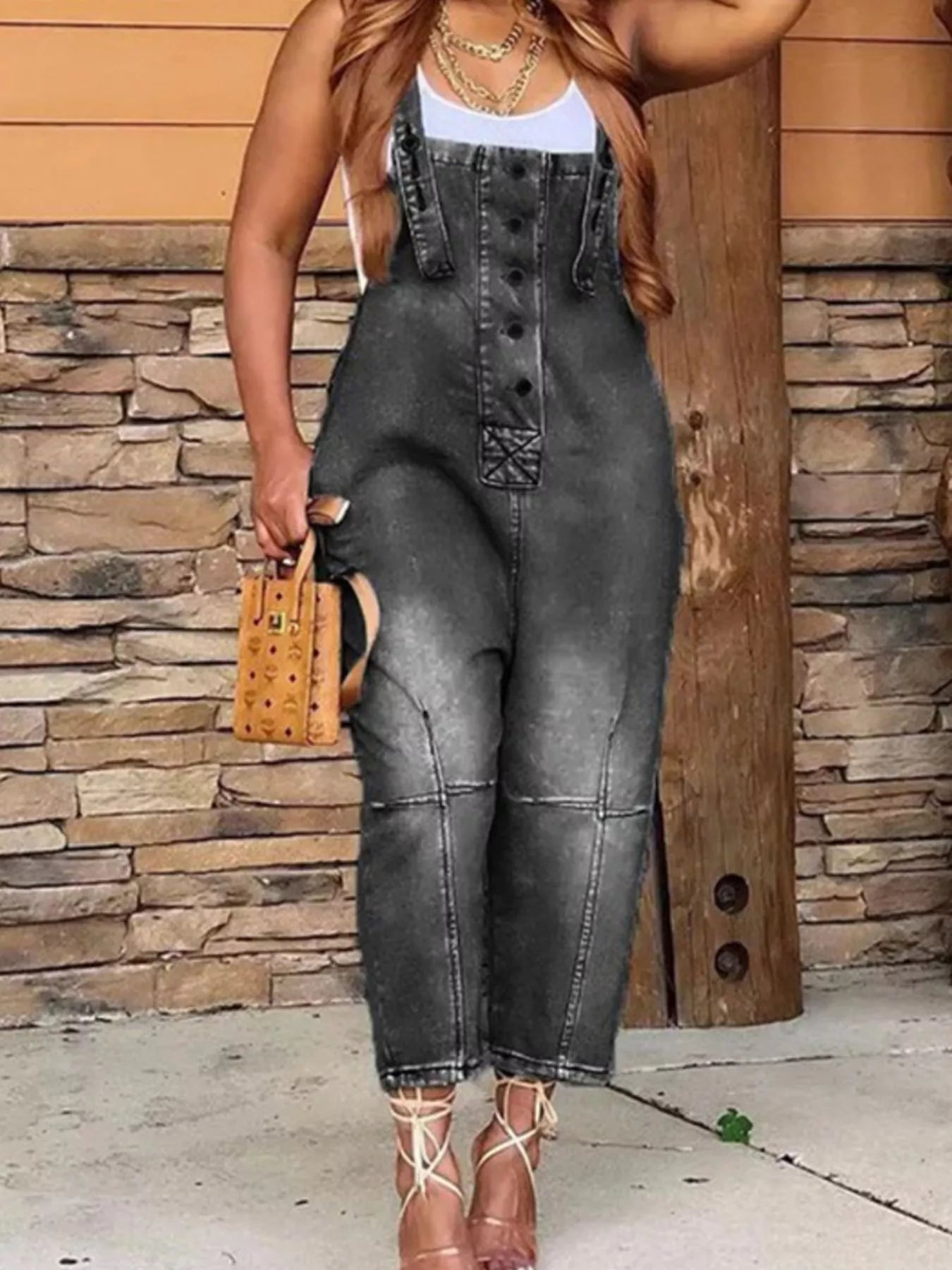Person wearing denim overalls standing against a stone wall.