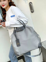 Woman holding a large gray bag with visible branding, standing in an indoor setting.
