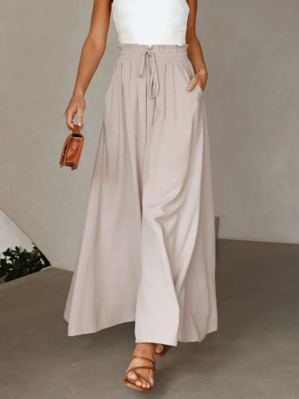 Person wearing a long beige skirt with a white top and brown sandals on a neutral background