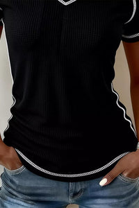 Black short-sleeve top with white trim worn by a person, paired with blue jeans.