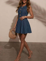 Woman wearing a blue dress with buttons, holding a beige handbag against a plain background