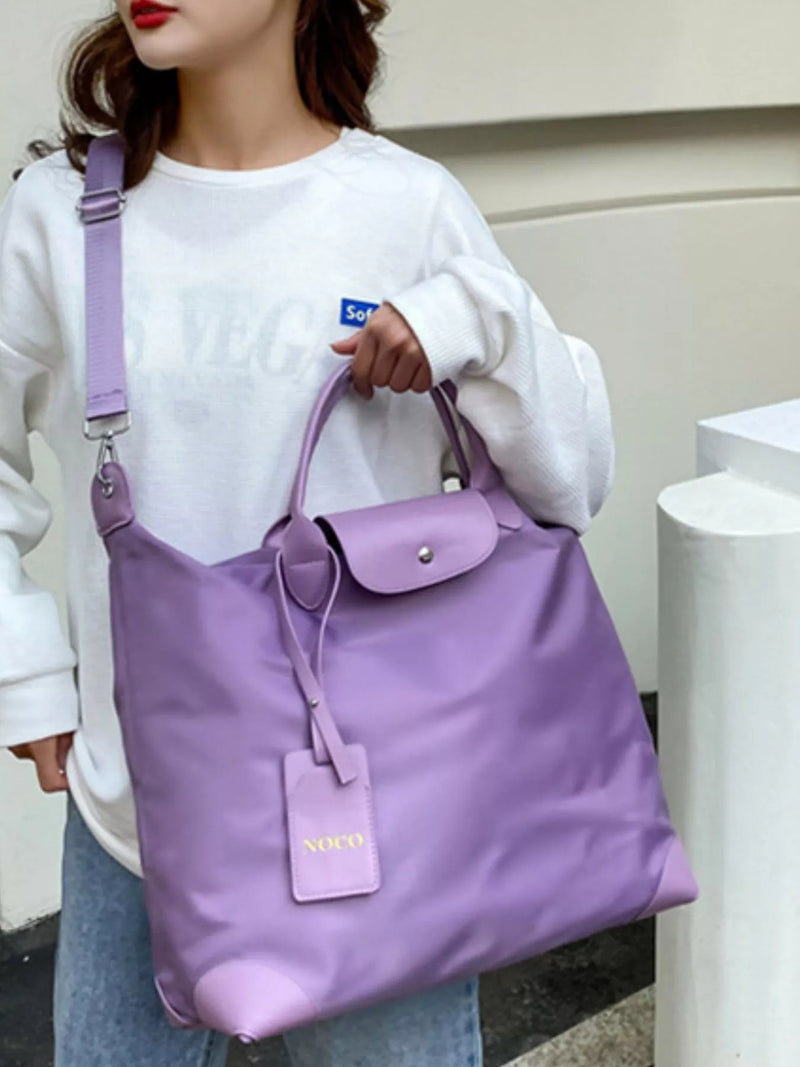 Person holding a purple handbag with a visible brand tag against a neutral background