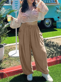 Person wearing a beige mesh top and wide-leg pants, holding a drink outdoors.