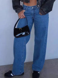 Person wearing blue jeans and a black jacket holding a black handbag against a plain background
