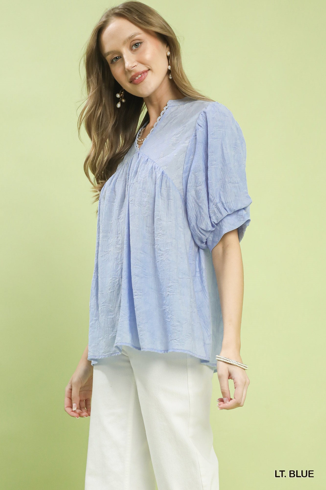 Woman wearing a light blue blouse with white pants on a light green background