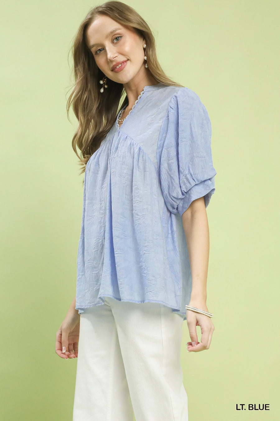 Woman wearing a light blue blouse with white pants on a light green background