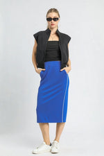 Woman wearing a black sleeveless jacket, black top, and blue skirt with white stripes on a white background
