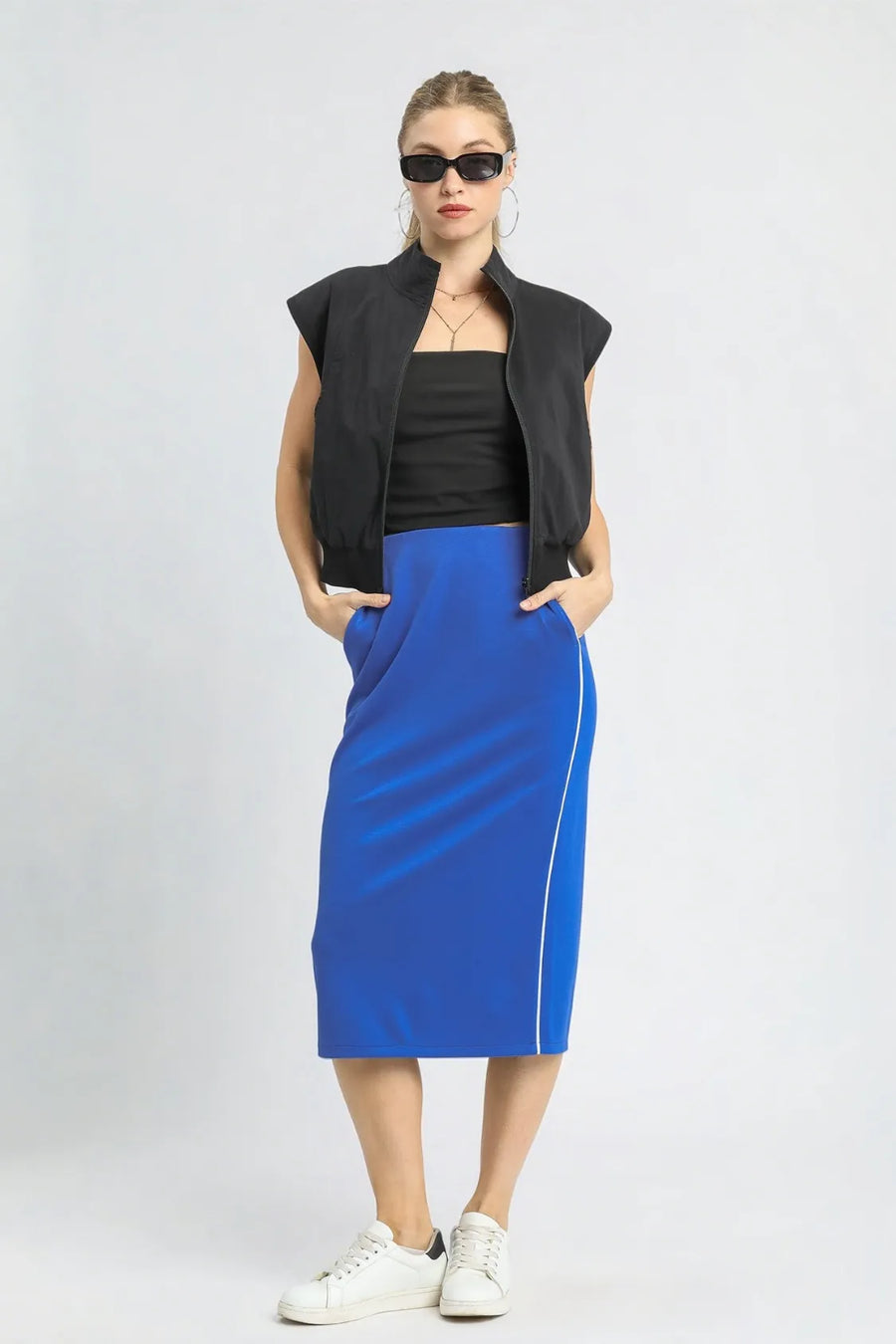 Woman wearing a black sleeveless jacket, black top, and blue skirt with white stripes on a white background