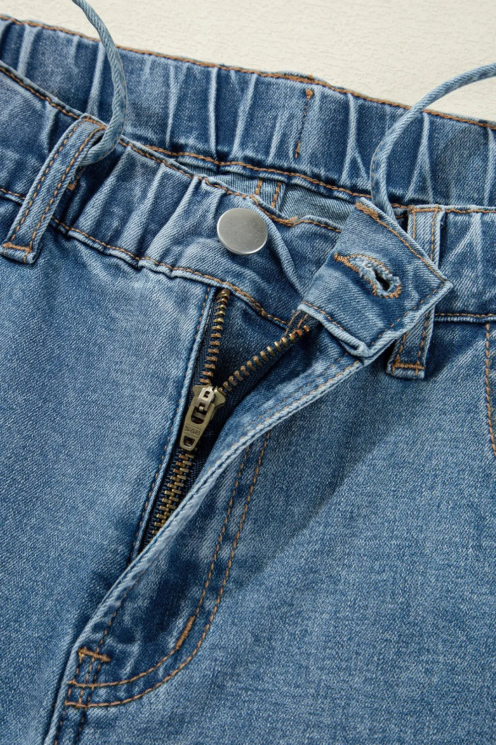 Close-up of a blue denim zipper and button on a garment.