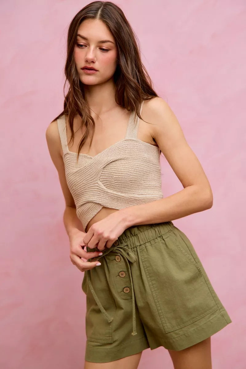 Woman wearing a beige knit top and green shorts against a pink background