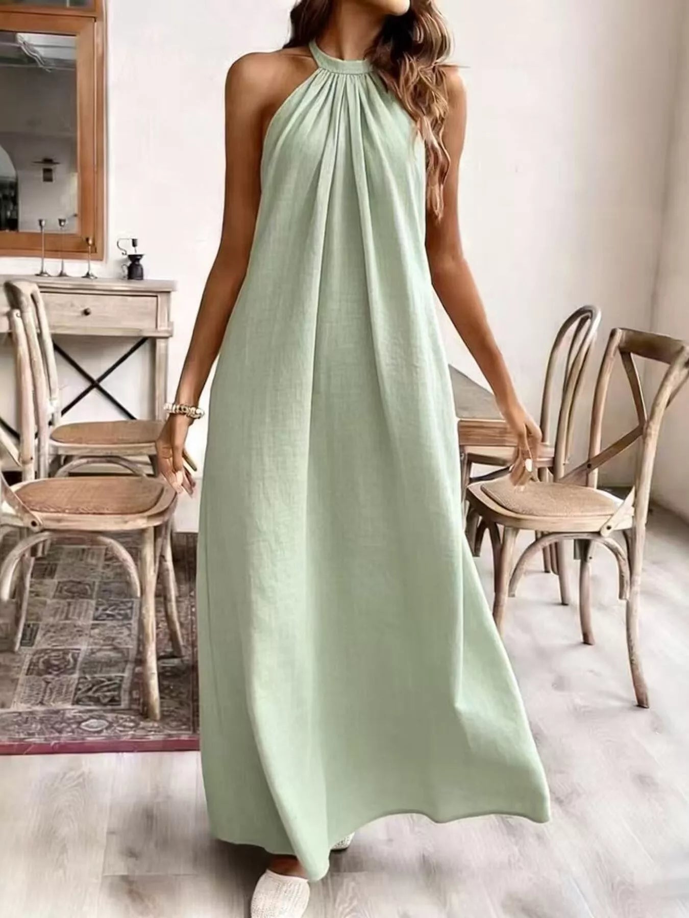 Woman wearing a light green dress in a room with wooden chairs and a mirror.