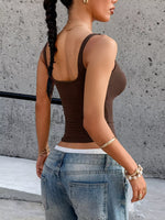 Person wearing a brown tank top and blue jeans against a concrete wall.