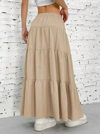 Beige tiered skirt worn by a person against a white brick wall.