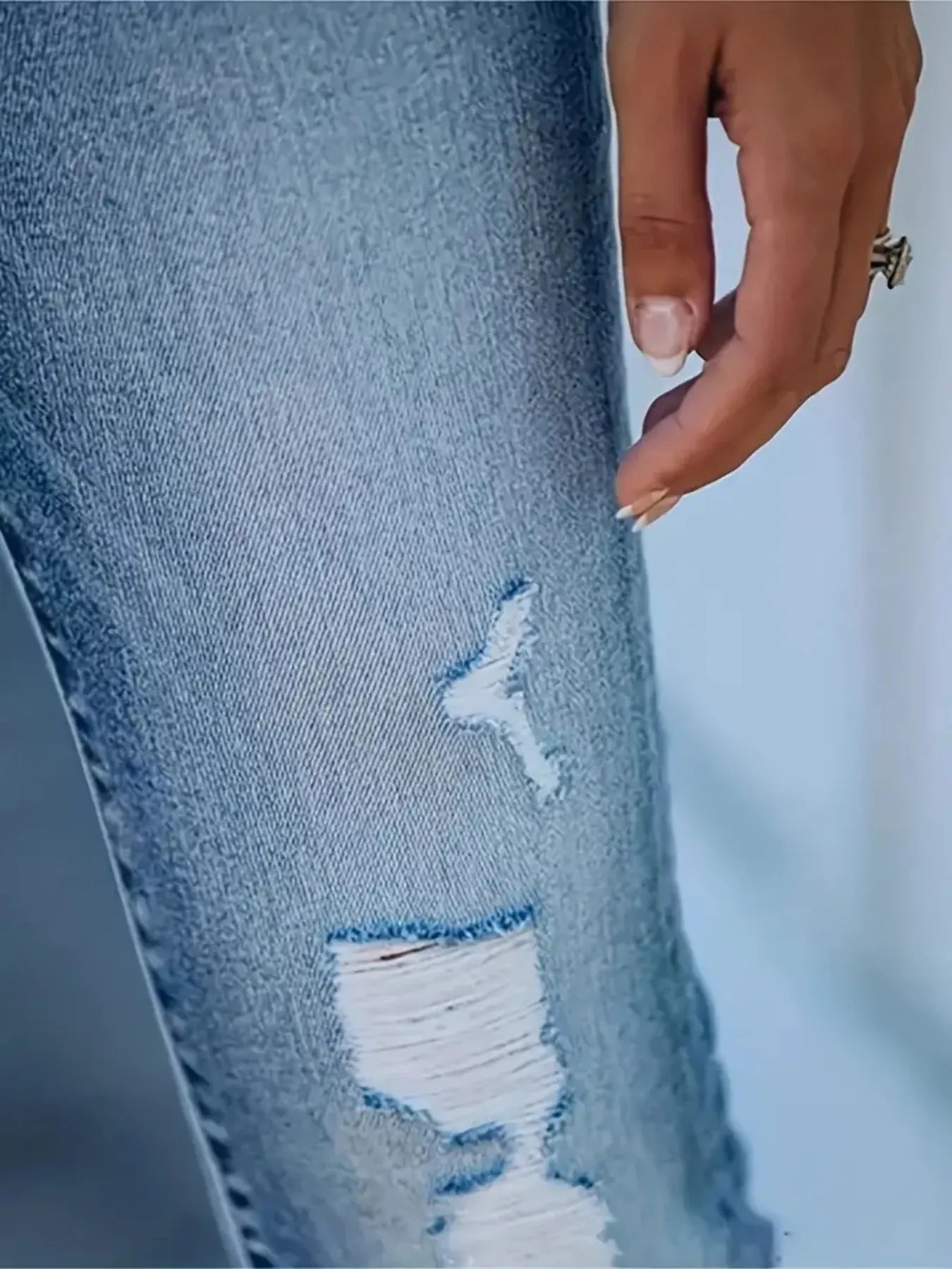 Close-up of a hand touching a distressed blue denim jeans with a blurred background