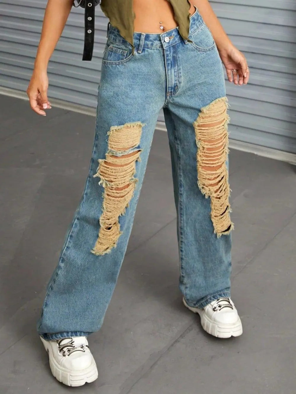 Person wearing distressed blue jeans with a plain background