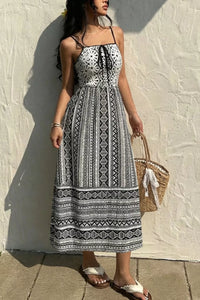 Woman wearing a black and white patterned dress against a light wall.