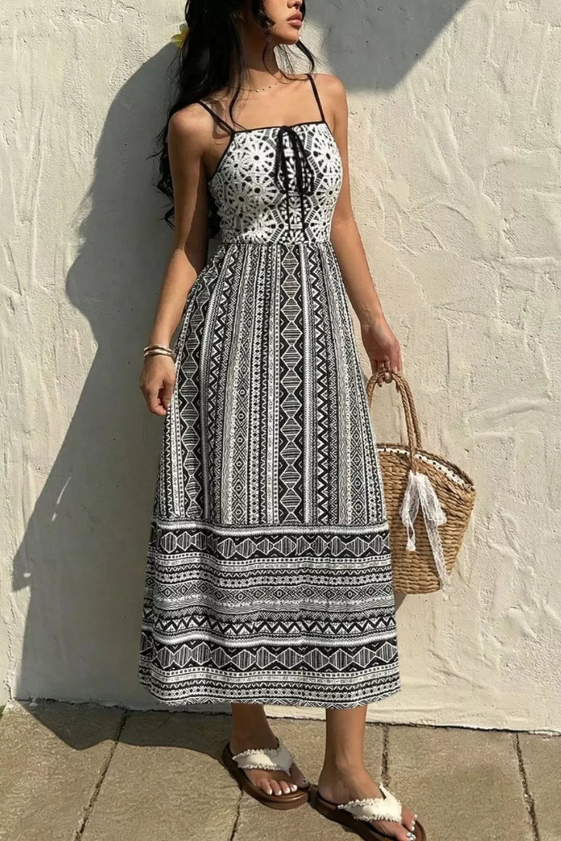 Woman wearing a black and white patterned dress against a light wall.