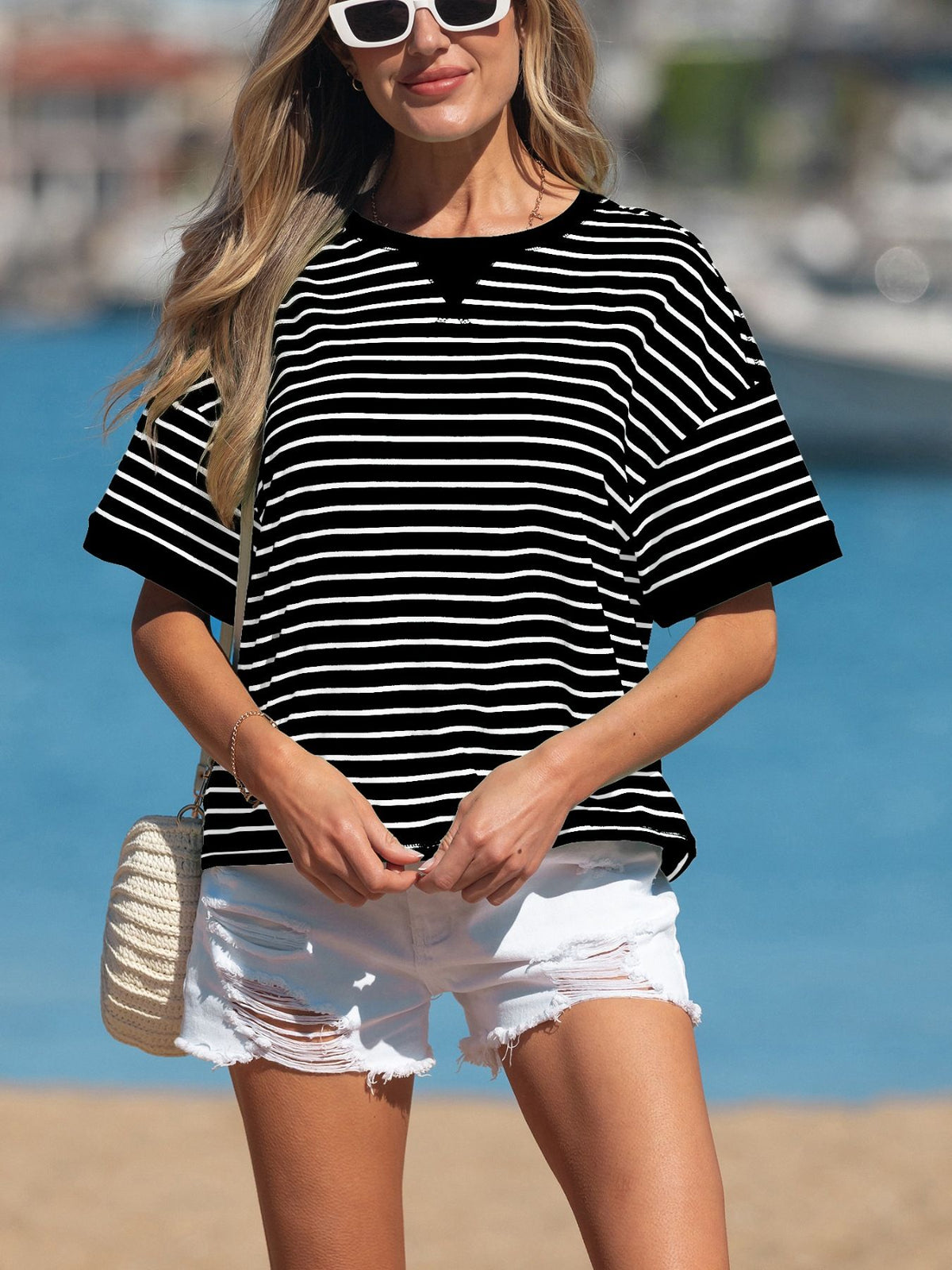 Woman wearing a black and white striped shirt and white shorts on a beach.