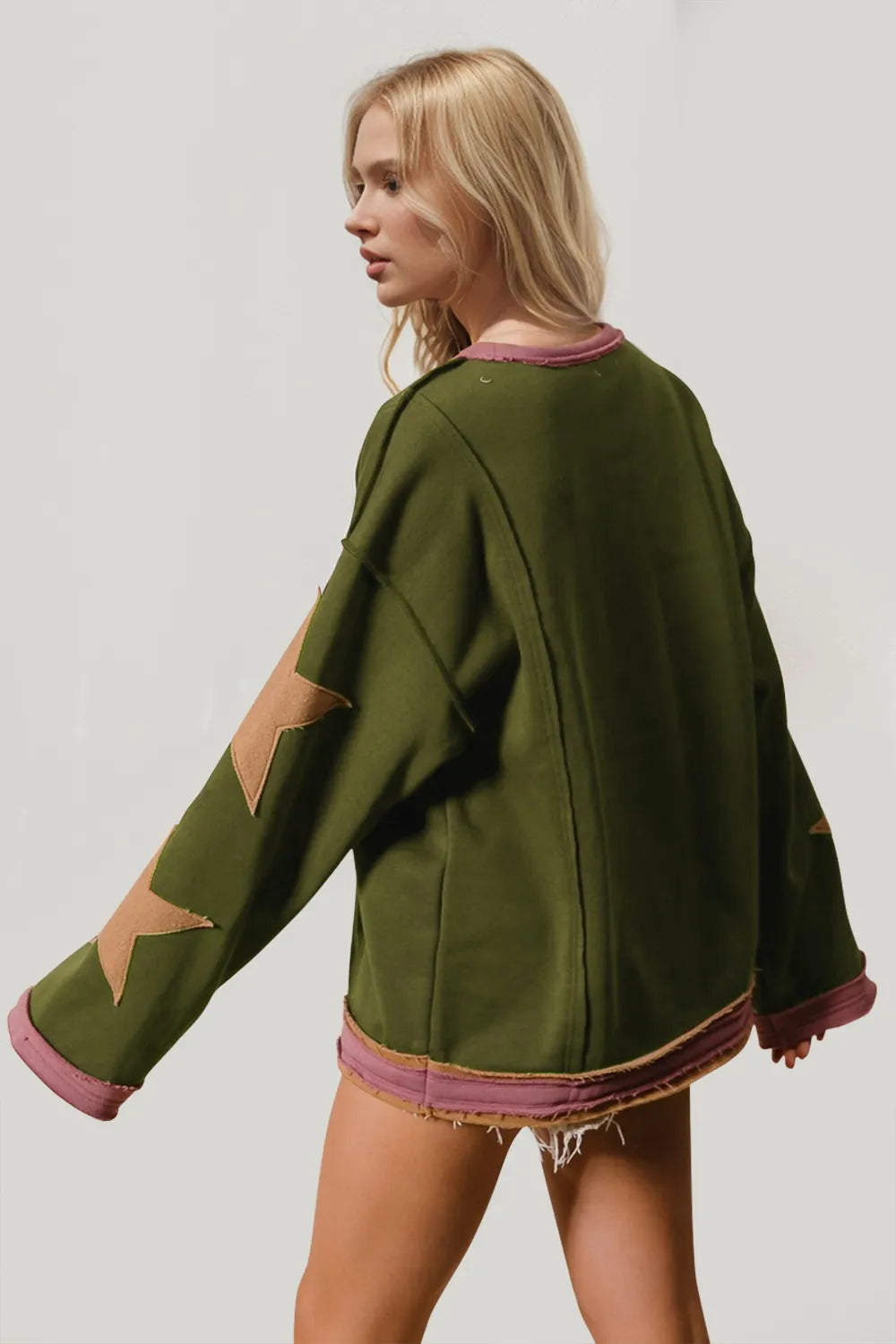 Woman wearing a green sweater with star designs on sleeves against a plain background