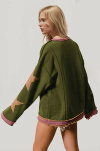 Woman wearing a green sweater with star designs on sleeves against a plain background