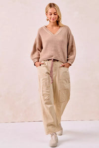 Woman wearing a beige sweater and pants against a plain background